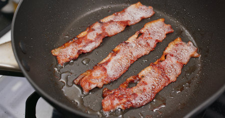 Cooking bacon on the fry pan in kitchen for breakfast