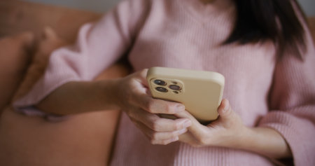 Woman use of smart phone and sit on sofa at homeの写真素材