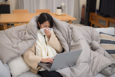 Woman get sick and sneeze with use of laptop computer at homeの写真素材