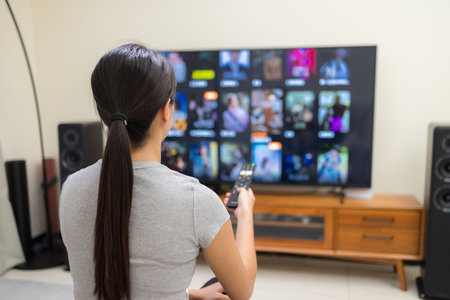 Woman watch TV and use remote control for choosing program at homeの写真素材