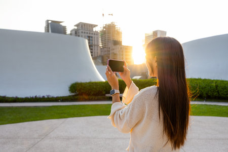 Woman use cellphone to take photo with sunlight flare under sunset