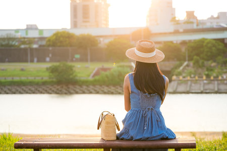 Woman with dress and straw hat sit on the bench at park under sunsetの写真素材
