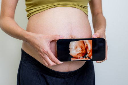 Pregnant woman show her ultrasound photo on cellphone with her tummy
