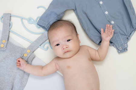 Newborn baby lying next to baby clothes