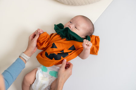 Mother Dressing Newborn in Halloween Pumpkin Outfitの写真素材