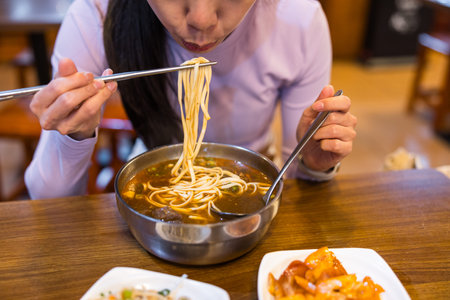 Young woman tasting delicious Taiwanese beef noodle soup