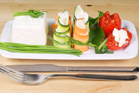 Cream cheese, Piccadilly tomatoes and zucchini and carrot rolls with cream cheese finely disposed on a white rectangular plate.の写真素材