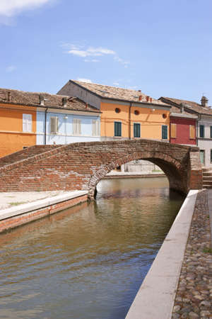 Stone arch bridge over a canal with colored houses behindの写真素材
