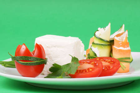 Cream cheese, Piccadilly tomatoes, zucchini and carrot rolls with cream cheese finely disposed on a squared white plate. Studio shot over green background.の写真素材