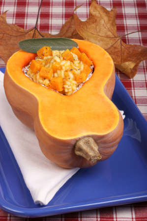 Half pumpkin filled with pumpkin risotto over a blue dishの写真素材