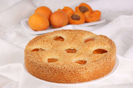 Apricot cake on a awhite cake stand. Apricots out of focus in the backgroundの写真素材
