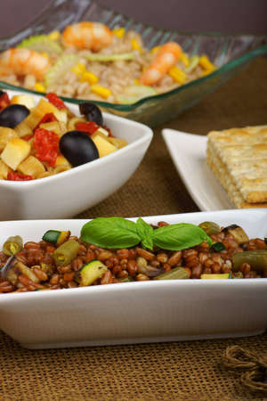 Spelt salad with eggplant, zucchini and green bean served in a white plate  Summer pasta salad and pearl barley salad out of focus int he background  Selective focus, shallow DOFの写真素材