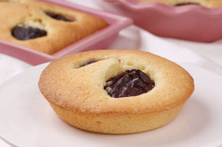 Small plum cake on a white cake stand  Plum cakes in pink pottery cake tins out of focus in the background  の写真素材
