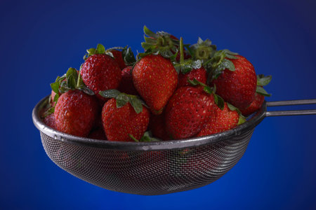 Fresh strawberries in a colander on a blue backgroundの写真素材
