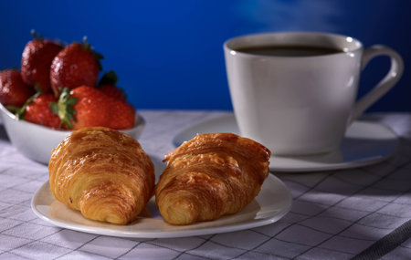 Croissants with coffee and strawberry on a blue backgroundの写真素材