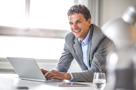 Portrait of smiling young businessman using laptop in officeの写真素材