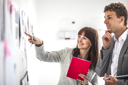 Young businesswoman with male colleague brainstorming at board in officeの写真素材
