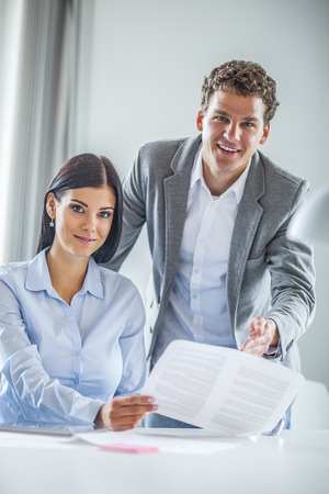 Portrait of happy young businesspeople discussing over document in officeの写真素材