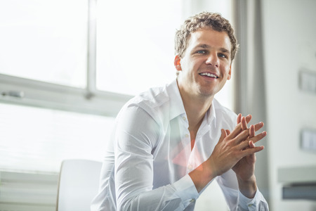 Thoughtful young businessman with hands clasped sitting in officeの写真素材