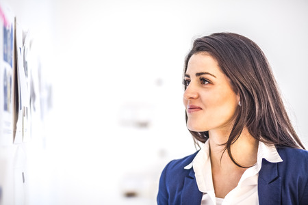 Young businesswoman reading papers on wall in creative office