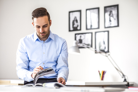 Young businessman analyzing brochures at desk in officeの写真素材