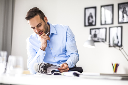 Young businessman analyzing brochure at desk in officeの写真素材