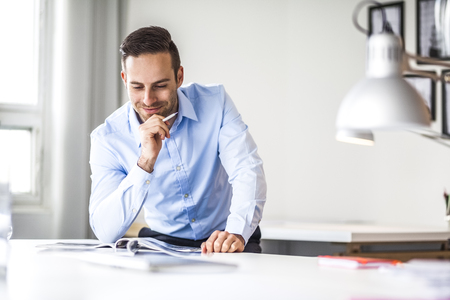 Confident young businessman analyzing brochure at desk in officeの写真素材