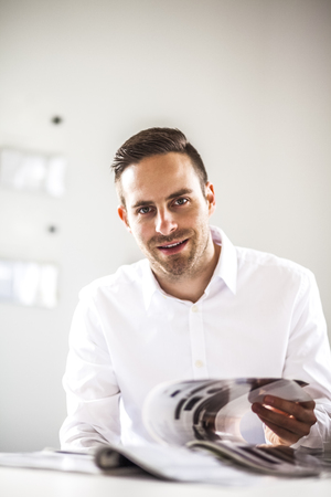 Portrait of young businessman analyzing brochure in officeの写真素材