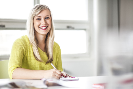 Portrait of smiling young businesswoman writing in diary at officeの写真素材