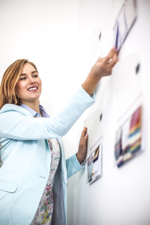 Young businesswoman sticking notes on wall in creative officeの写真素材