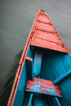 The front of a colourful wooden canoe cuts through the still water of Phewa (Fewa) Lake in Pokhara, Nepal.の写真素材
