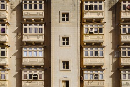 Rows of identical stone coloured wooden Maltese traditional balconies in harsh sunlight. Valletta social housing.の写真素材