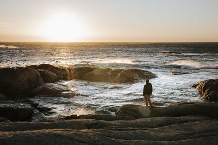Adult male looking off into the distant ocean at sunset. Calm and peace, inspirational scene.