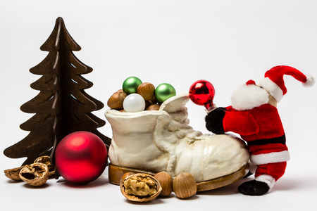 Santa Claus fills a shoe with gifts. Next to it is a brown fir tree on white background.の写真素材