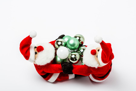 Two Santas sit in front of a white background and hold small Christmas ballsの写真素材