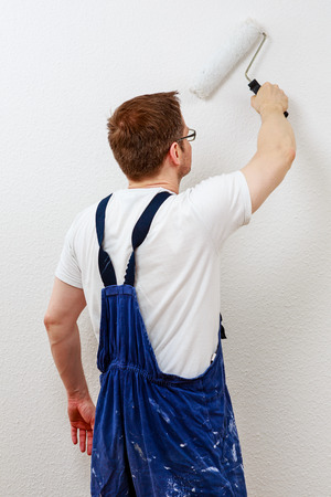 Man in blue overall painting a wall whiteの写真素材