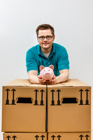happy man holds his piggy bank high, in his new apartment.の写真素材