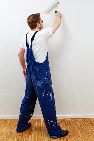 Man in blue overall painting a wall whiteの写真素材