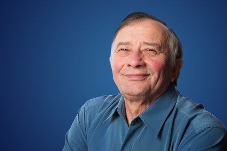 Senior man with a friendly smile standing against a blue background