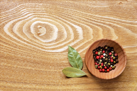 Fragrant colorful pepper in a wooden bowl and two dried bay leaves on a light wooden table. Top view.の写真素材
