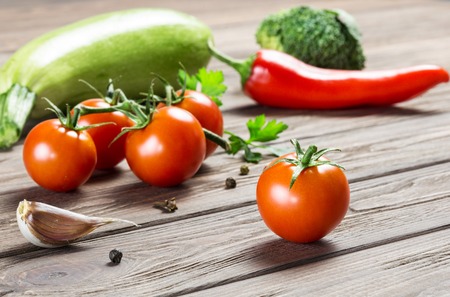 Ripe cherry tomatoes, garlic cloves, zucchini, greens, broccoli and a little pepper on a wooden surface.の写真素材