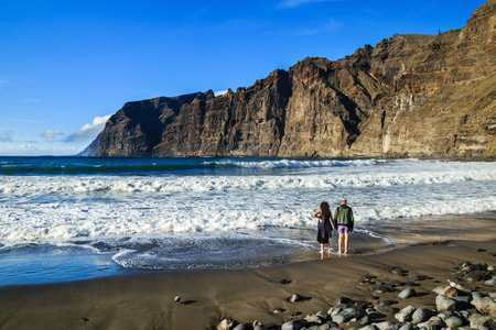 Los Gigantes, Tenerife, Spain - Fabruary 16, 2019: Couple of people on the ocean coast against the Acantilados de Los Gigantes cliffs, the famous tourist attraction in the northwest part of island.のeditorial素材