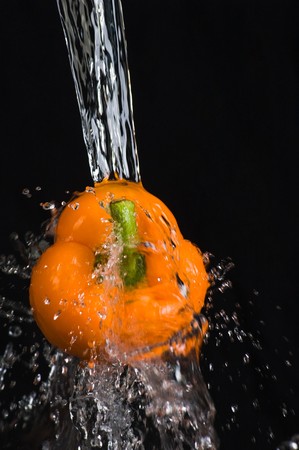 orange bell pepper in water stream on black backgroundの写真素材