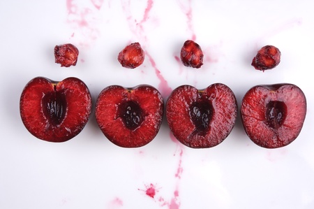 image of fresh cherries cut in halves with seeds  and cherry juice on whiteの写真素材