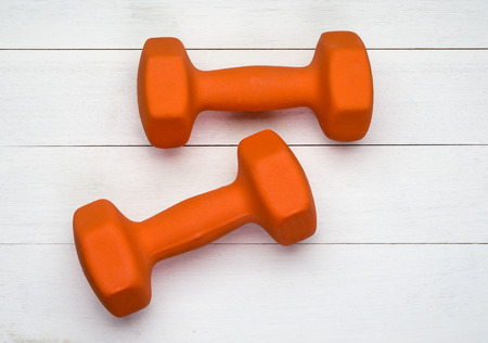 Two orange plastic coated dumbbells on white wooden backgroundの写真素材