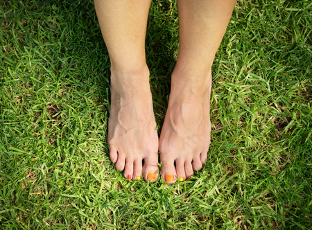 female feet with multi colored pedicure on the green grass
