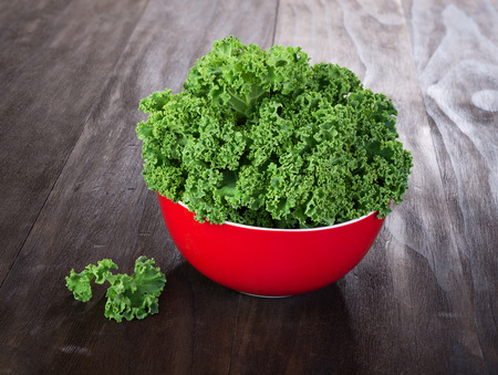 fresh green kale leaves in red ceramic bowl on vintage wooden tableの写真素材
