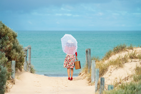 Beautiful woman traveler in retro style dress  on the beach. Local focus on the womanの写真素材