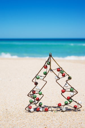 Small metal Christmas tree with jingle bells on the beach.
New Year and Christmas holiday conceptの写真素材