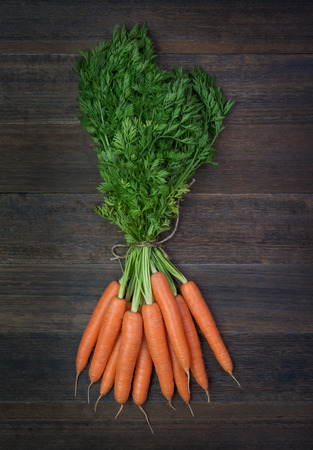 Bunch of fresh carrots vegetables with green leaves on rustic wooden backgroundの写真素材